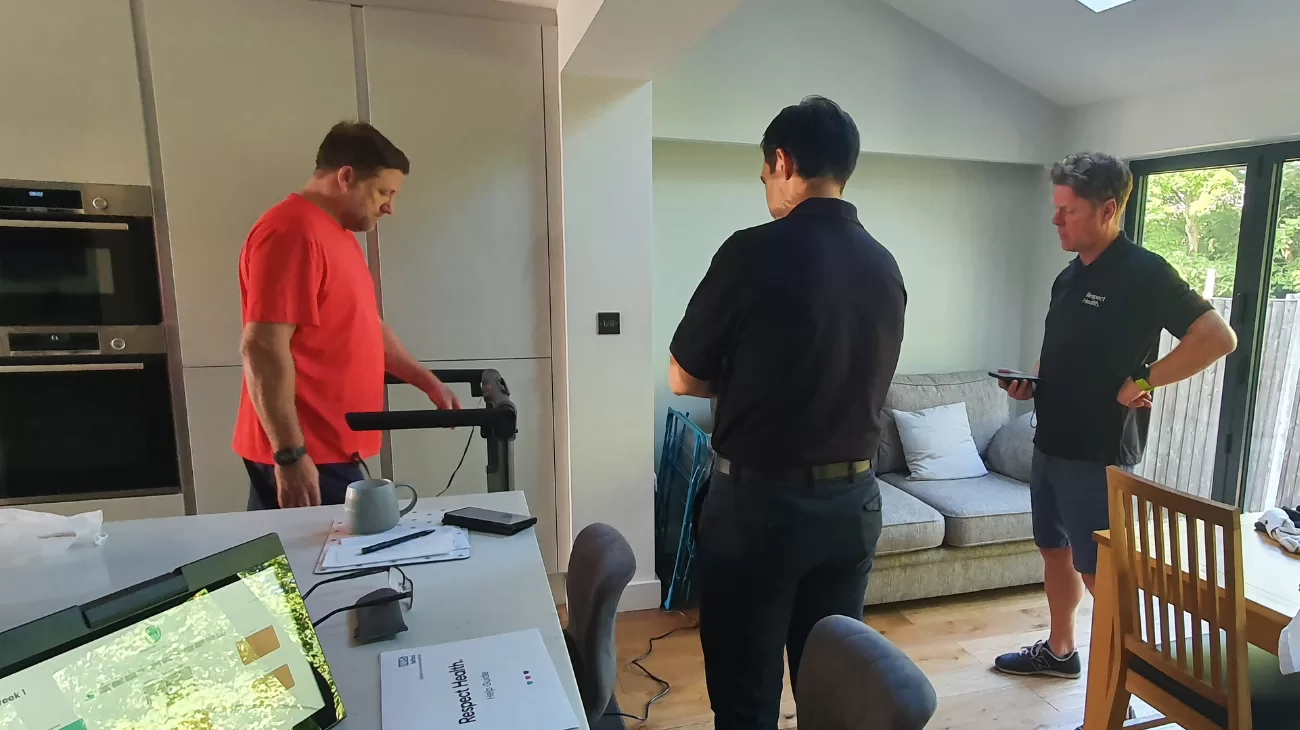 A participant of the Salford home exercise programme using a treadmill in their living room, watched by two of the programme's coaches