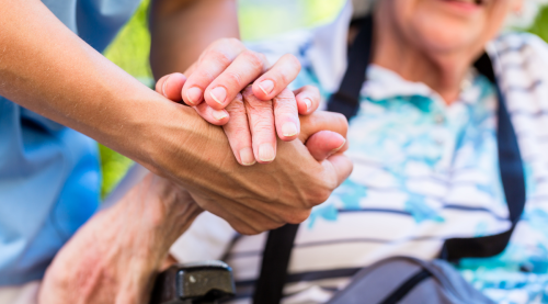Close up of someone clasping hands with a person sitting in a wheelchair.