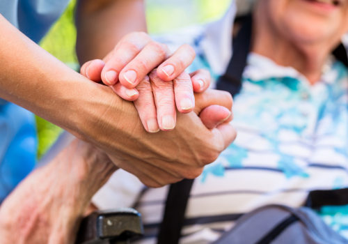 Close up of someone clasping hands with a person sitting in a wheelchair.