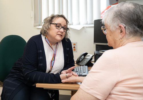 Care coordinator Cheryl sitting at a desk in a consulting room and talking to patient who is sitting opposite.