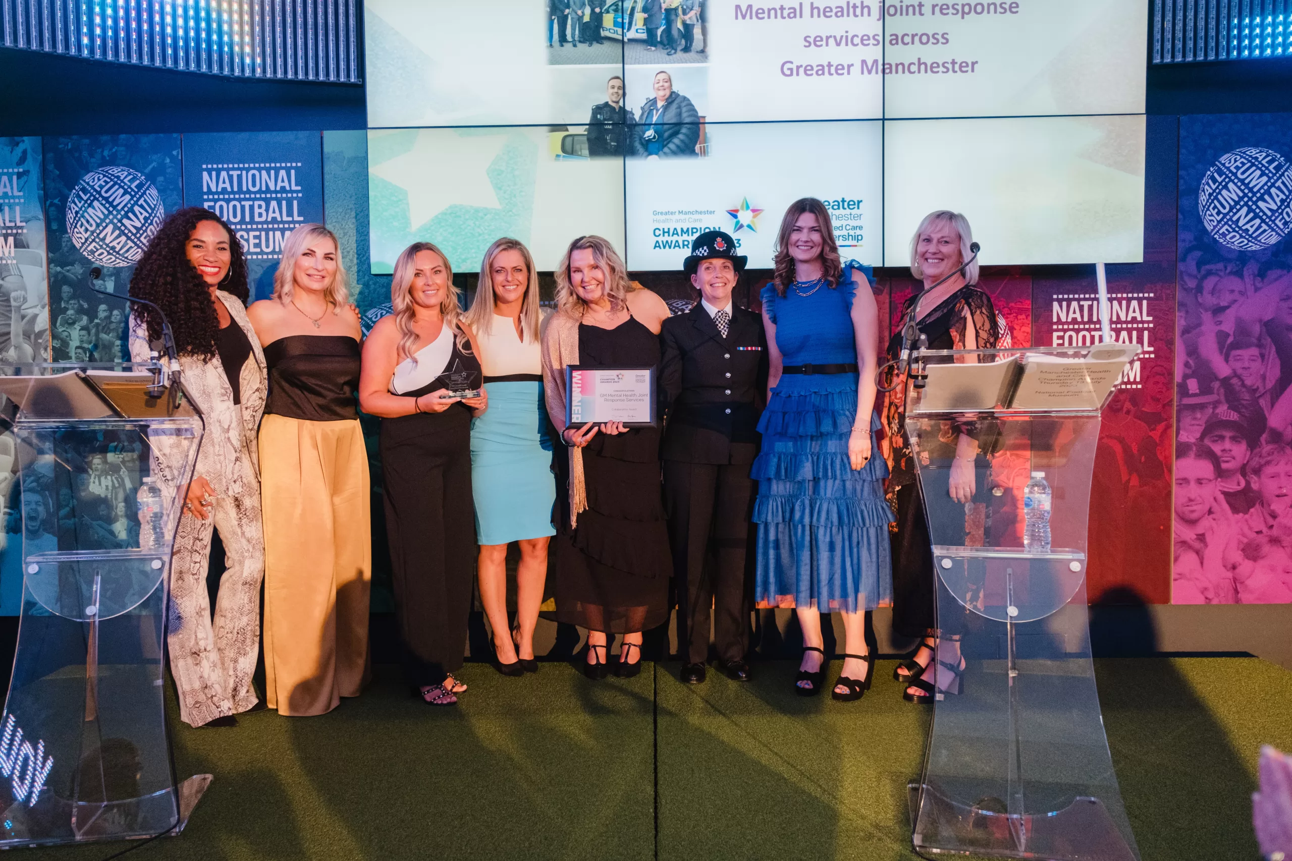a group of 8 people up on the stage with 5 being presented with the award
