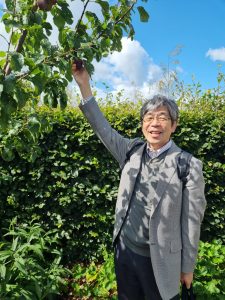 A smiling Dr Masanaga Yamawaki pictured against a backdrop of green trees and bushes at RHS Bridgewater Hall