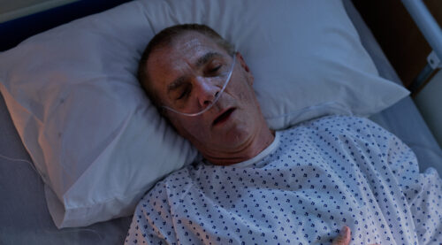 A person lying in a hospital bed with a tube attached to their nose to help them breathe.