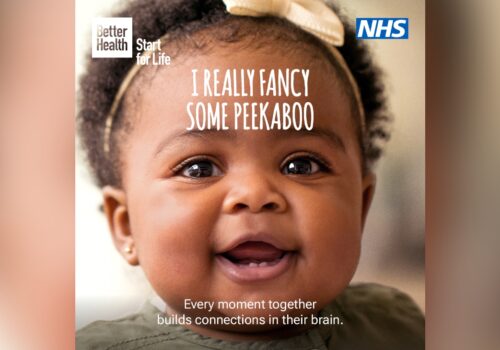 Campaign image. Close up of a smiling healthy baby. I really fancy some peekaboo. Every moment together builds connections in their brain.