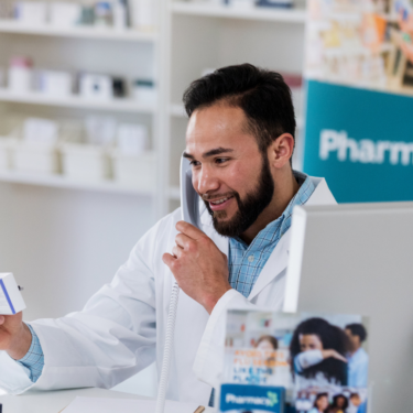 Pharmacist working in a pharmacy on the telephone looking at a box of medication.
