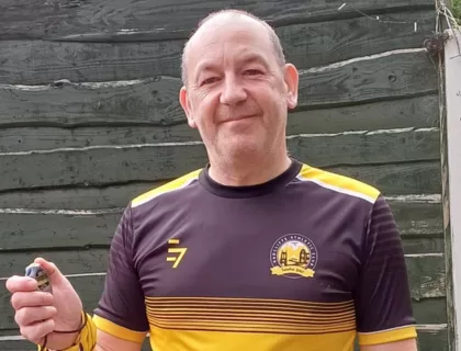A person wearing a yellow and black Radcliffe Athletic Club T-shirt holding a stopwatch.