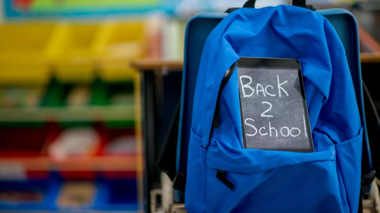 A backpack adorned with a note "back 2 school" sits in a classroom.