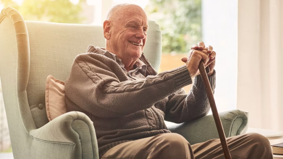 An elderly person sitting in an armchair smiling