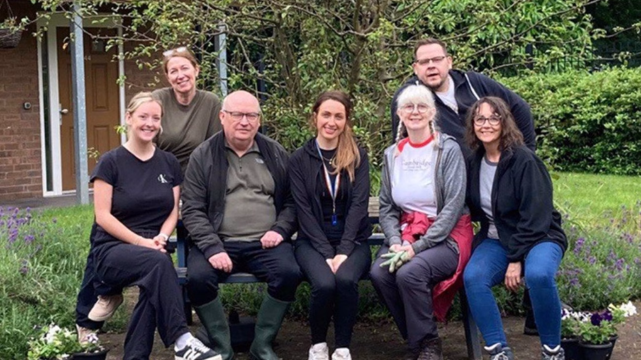 A group of people sat in a row in a garden. They have been volunteering at a community housing project.