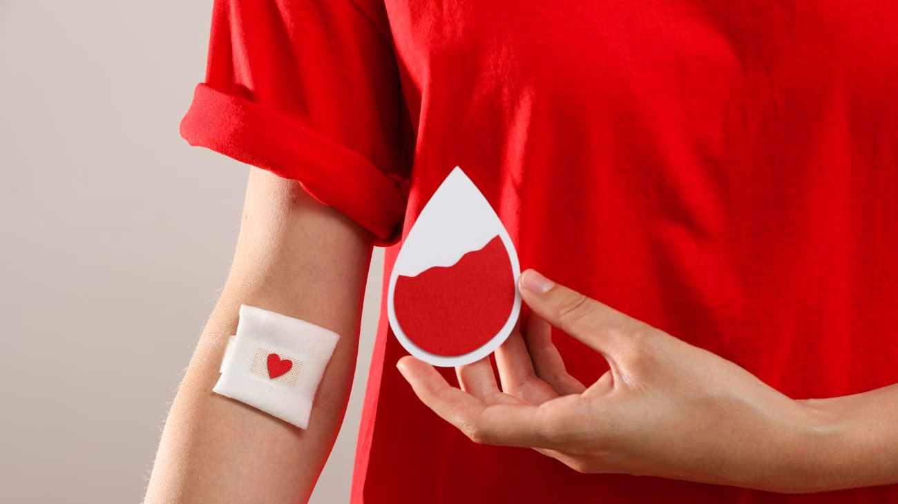 Give blood. A person with a plaster on their arm having just given blood is holding a red drop of blood.