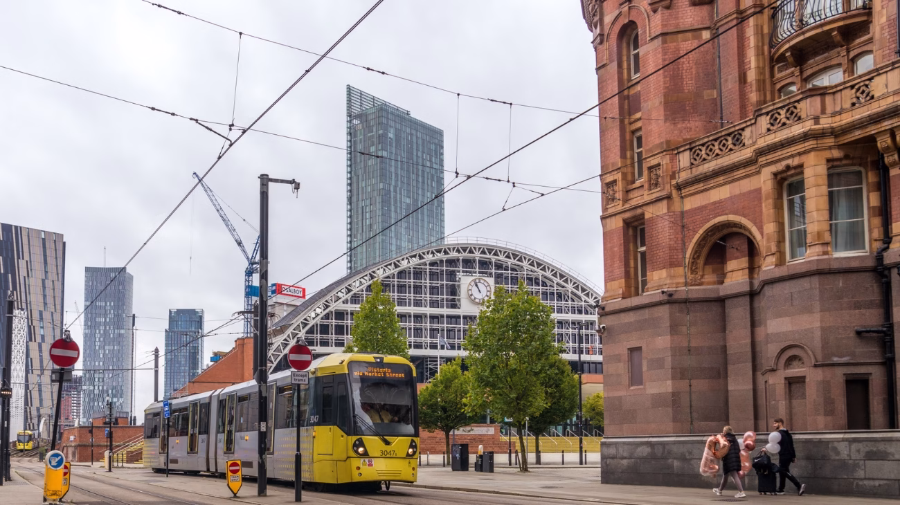 A shot of a busy Manchester street with a tram in the background. You can see Manchester Central convention centre in the background where the NHS ConfedExpo event is being held.