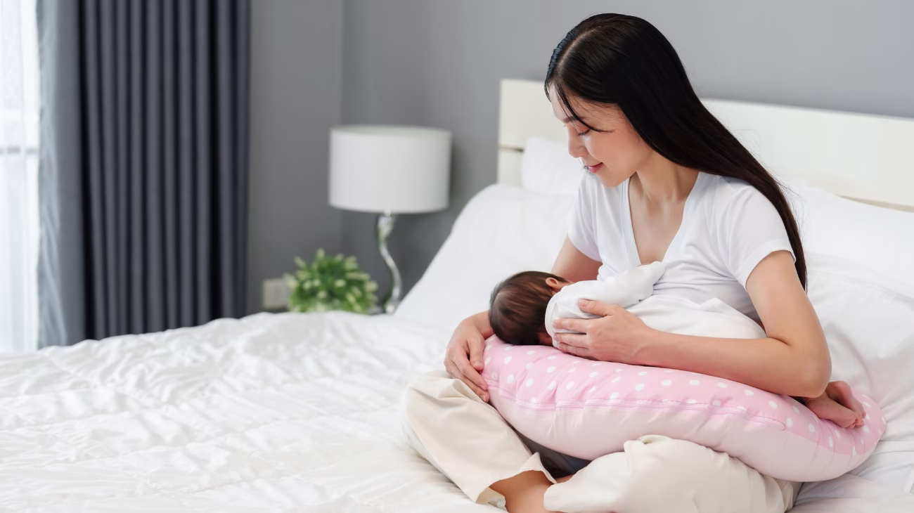 A person sat on a bed breastfeeding their infant.