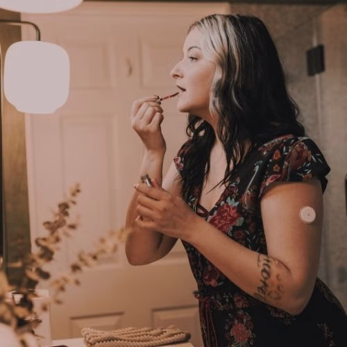 Winter vaccinations. A young person getting ready in the mirror. They have a diabetes monitoring system on their arm.