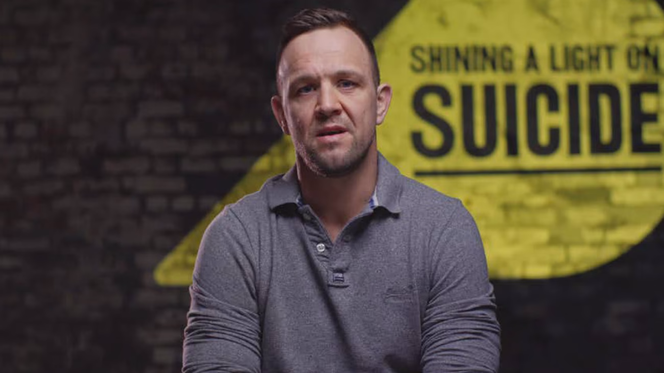 A man sat in front of a camera looking directly down the camera.