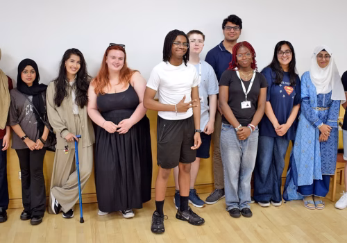 A group of young people standing in a line as they smile at the camera. They are members of Bee Heard and helped to create the Greater Manchester Youth Health Agreement.