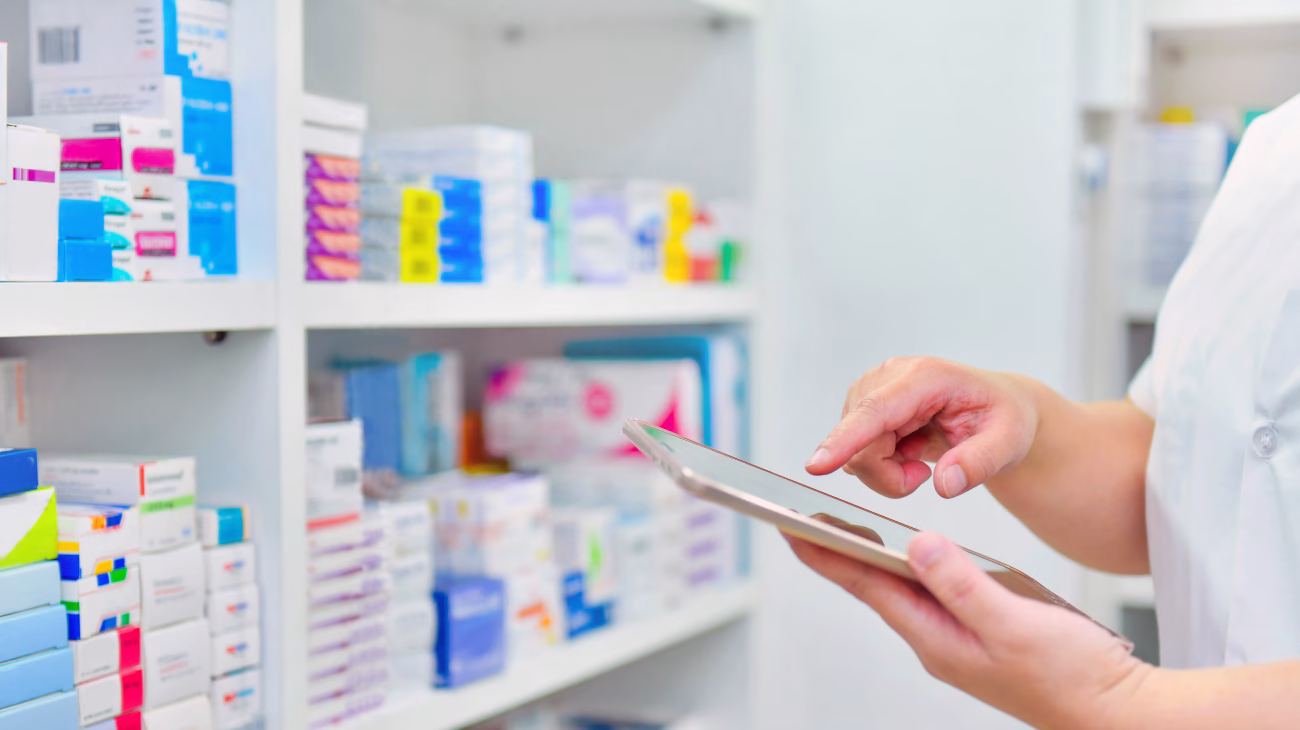 A person stood holding a device with pharmacy shelves in the background.