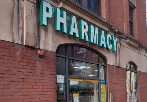 A green and white pharmacy sign over double glass entrance doors.