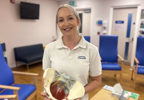 A physiotherapist is stood posing for a picture holding a part of a skeleton.