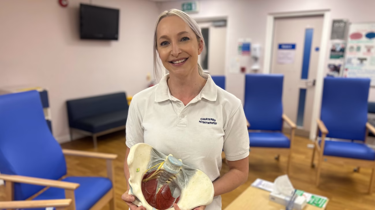 A physiotherapist is stood posing for a picture holding a part of a skeleton.