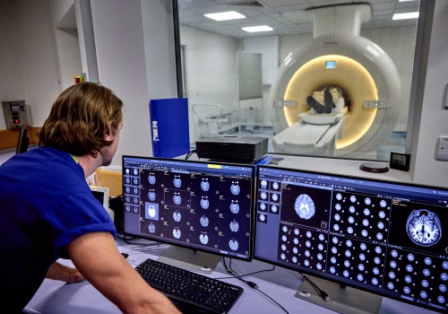 Person in an MRI machine while a clinician looks at scans of their brain