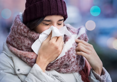Person in a beanie, scarf and coat sneezing into a tissue
