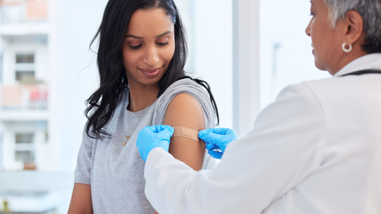 Clinician putting a plaster on a young persons arm where they got vaccinated